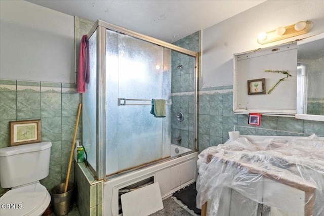 bathroom featuring toilet, shower / bath combination with glass door, and tile walls