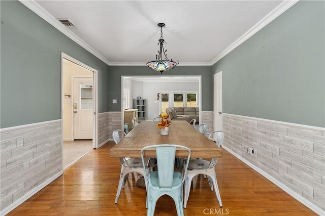 dining area featuring crown molding, tile walls, and light wood-type flooring