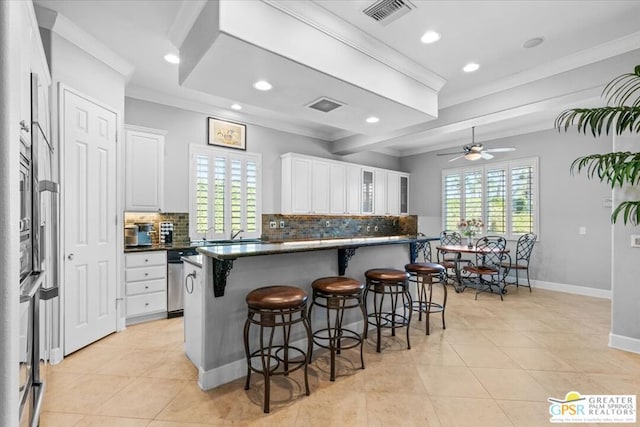 kitchen with a breakfast bar, ceiling fan, crown molding, dishwasher, and white cabinetry