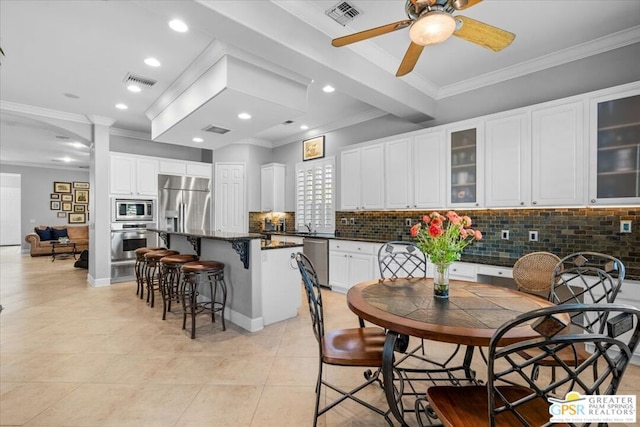 kitchen with ceiling fan, a kitchen island, built in appliances, white cabinets, and ornamental molding