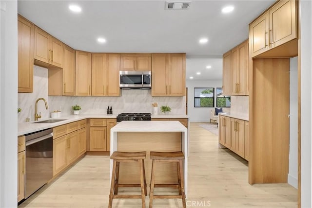 kitchen featuring decorative backsplash, appliances with stainless steel finishes, sink, light brown cabinets, and light hardwood / wood-style flooring