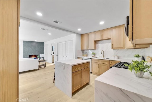 kitchen with tasteful backsplash, sink, light brown cabinets, a center island, and light hardwood / wood-style floors