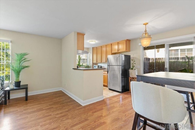 kitchen with stainless steel refrigerator, a wealth of natural light, light hardwood / wood-style flooring, and light brown cabinets