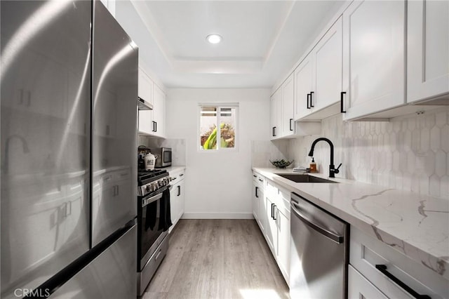 kitchen featuring white cabinets, sink, light stone countertops, light hardwood / wood-style floors, and stainless steel appliances