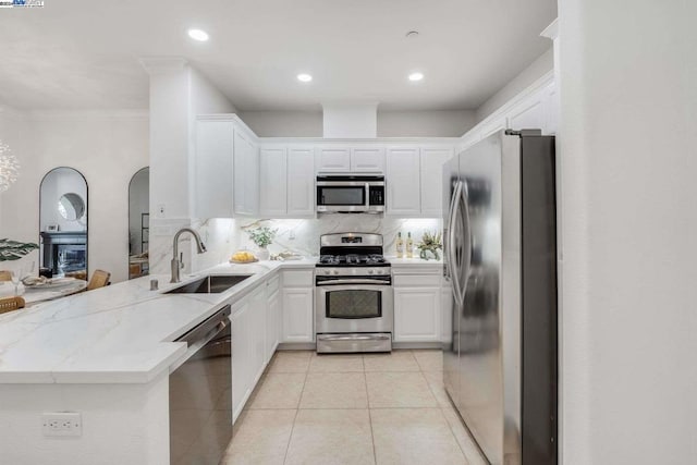 kitchen with sink, light stone counters, kitchen peninsula, white cabinets, and appliances with stainless steel finishes