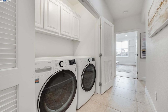 clothes washing area featuring washer and dryer, light tile patterned flooring, and cabinets