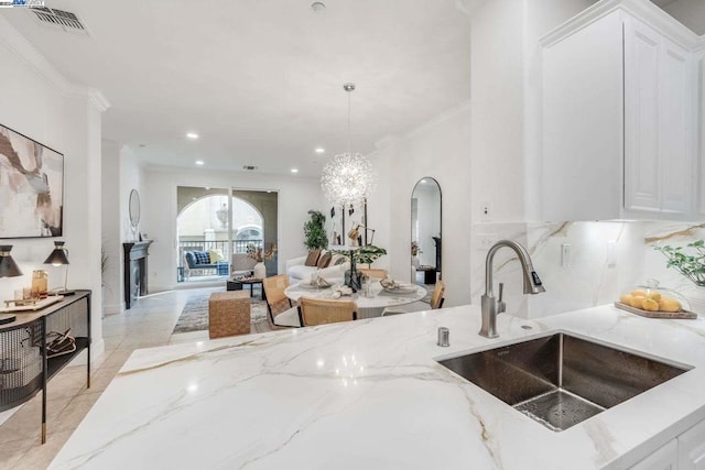 kitchen featuring crown molding, sink, decorative light fixtures, light stone counters, and white cabinetry