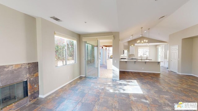 unfurnished living room with a tiled fireplace, vaulted ceiling, a healthy amount of sunlight, and sink