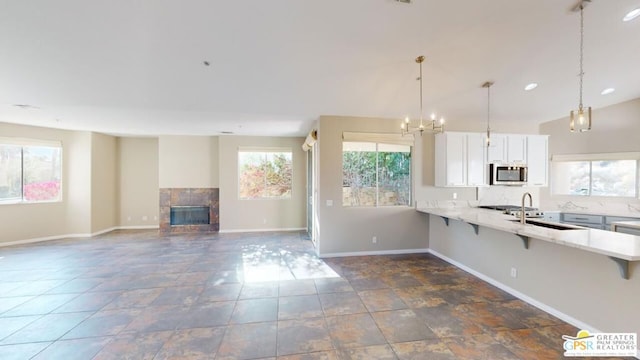 kitchen featuring pendant lighting, white cabinetry, a kitchen breakfast bar, and a tiled fireplace