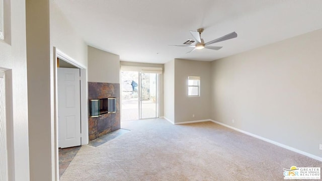 unfurnished living room featuring ceiling fan, a tiled fireplace, and light colored carpet