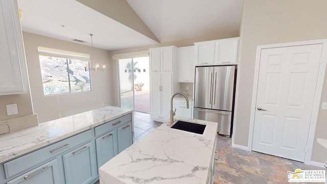 kitchen with lofted ceiling, sink, hanging light fixtures, stainless steel fridge, and white cabinets