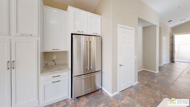 kitchen with white cabinetry, high quality fridge, vaulted ceiling, and light stone counters