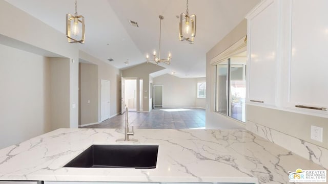 kitchen with pendant lighting, sink, a chandelier, and light stone counters