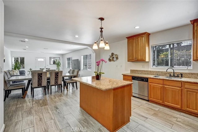 kitchen with stainless steel dishwasher, sink, decorative light fixtures, light hardwood / wood-style floors, and a kitchen island