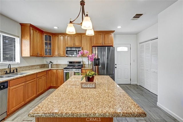 kitchen with appliances with stainless steel finishes, light wood-type flooring, sink, pendant lighting, and a kitchen island