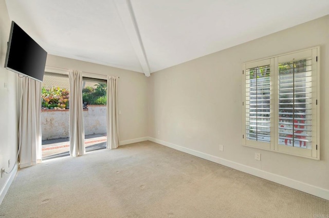 empty room featuring plenty of natural light, lofted ceiling with beams, and light colored carpet