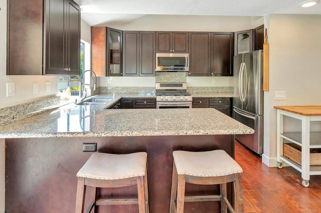 kitchen featuring sink, a kitchen breakfast bar, dark hardwood / wood-style floors, kitchen peninsula, and appliances with stainless steel finishes