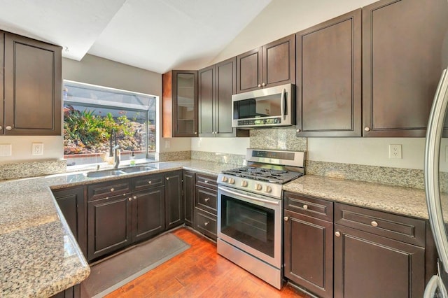 kitchen with appliances with stainless steel finishes, dark hardwood / wood-style flooring, light stone counters, sink, and lofted ceiling