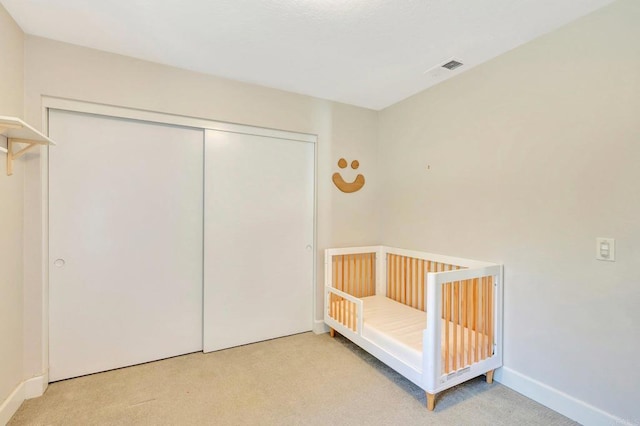 unfurnished bedroom with a crib, light carpet, and a closet