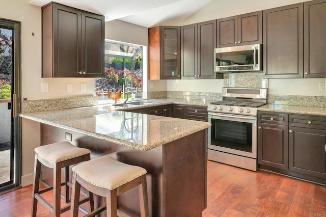 kitchen with kitchen peninsula, dark hardwood / wood-style flooring, a breakfast bar, and appliances with stainless steel finishes