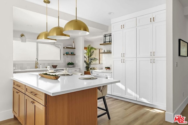 kitchen with pendant lighting, sink, a breakfast bar, light hardwood / wood-style floors, and white cabinets