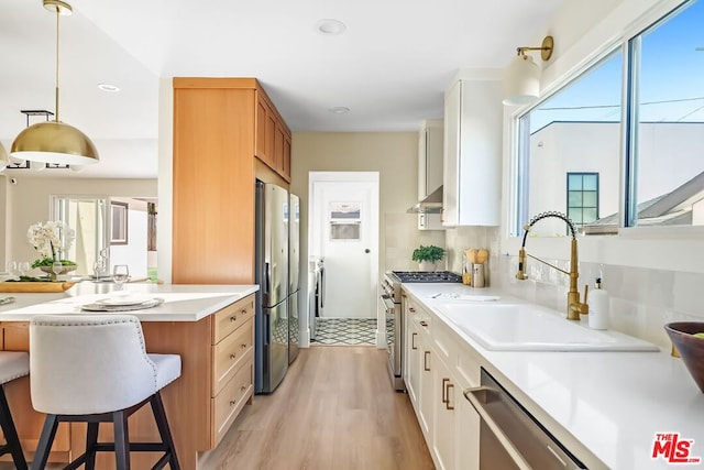 kitchen featuring sink, light wood-type flooring, appliances with stainless steel finishes, pendant lighting, and white cabinets