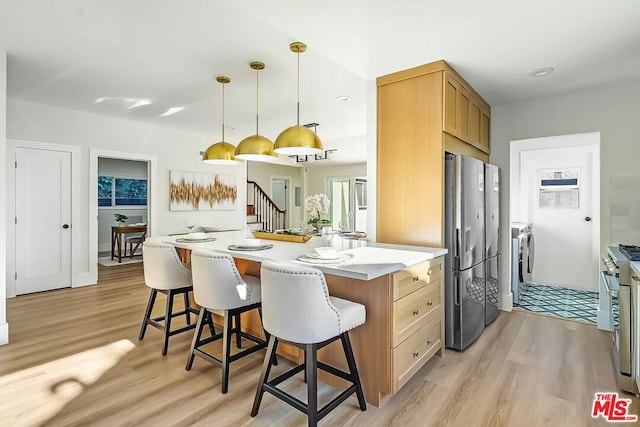 kitchen with a breakfast bar area, hanging light fixtures, stainless steel appliances, separate washer and dryer, and light wood-type flooring