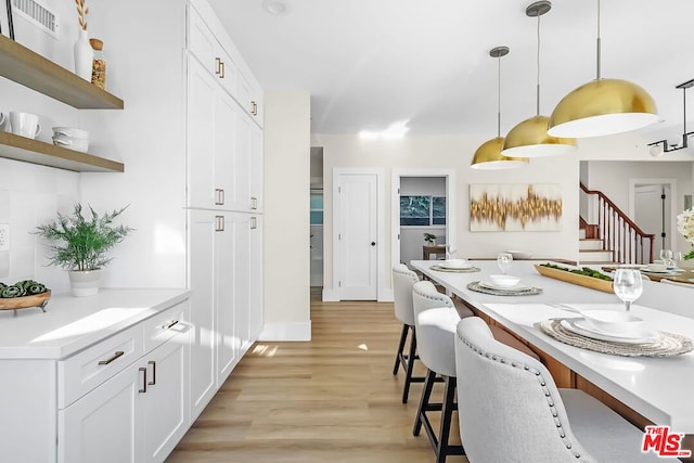 kitchen with white cabinetry, a breakfast bar area, pendant lighting, and light hardwood / wood-style flooring