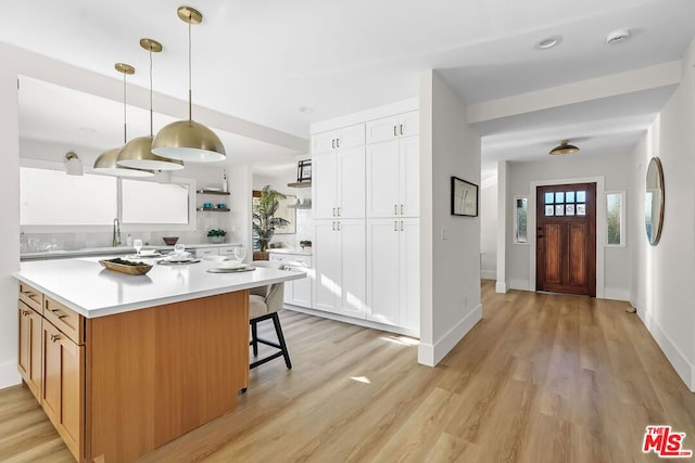 kitchen featuring sink, light hardwood / wood-style flooring, white cabinets, a kitchen bar, and decorative light fixtures