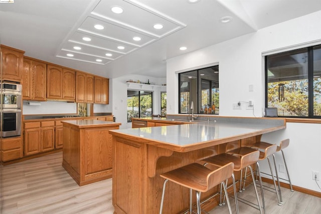 kitchen with kitchen peninsula, light wood-type flooring, stainless steel double oven, a center island, and a breakfast bar area