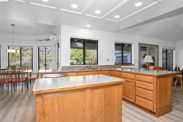 kitchen with a center island, sink, light hardwood / wood-style floors, decorative light fixtures, and a kitchen bar