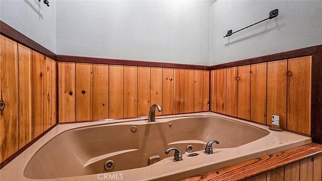 bathroom featuring wooden walls and a tub