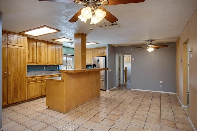 kitchen with sink, stainless steel fridge, a kitchen bar, light tile patterned floors, and ceiling fan