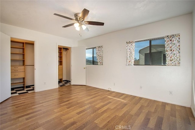 unfurnished bedroom with multiple closets, ceiling fan, and wood-type flooring