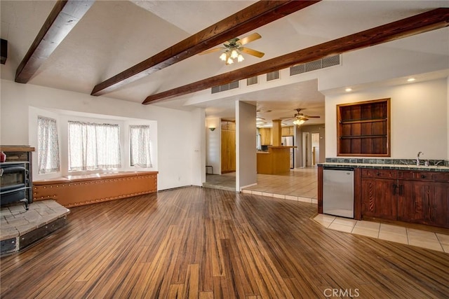 living room with lofted ceiling with beams, a wood stove, sink, ceiling fan, and light hardwood / wood-style floors