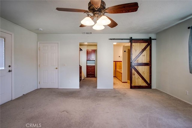 unfurnished bedroom with ceiling fan, a barn door, light colored carpet, and ensuite bath