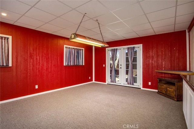 basement with french doors, wood walls, carpet, and a drop ceiling