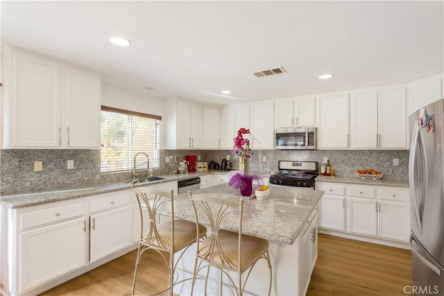 kitchen with white cabinets, sink, light hardwood / wood-style flooring, appliances with stainless steel finishes, and a kitchen island