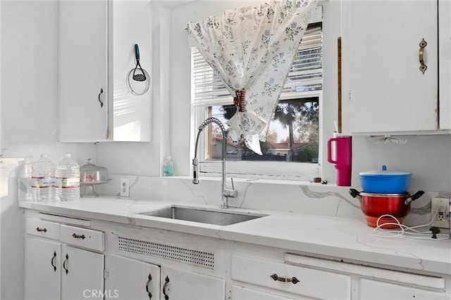 kitchen featuring plenty of natural light, sink, white cabinets, and light stone counters