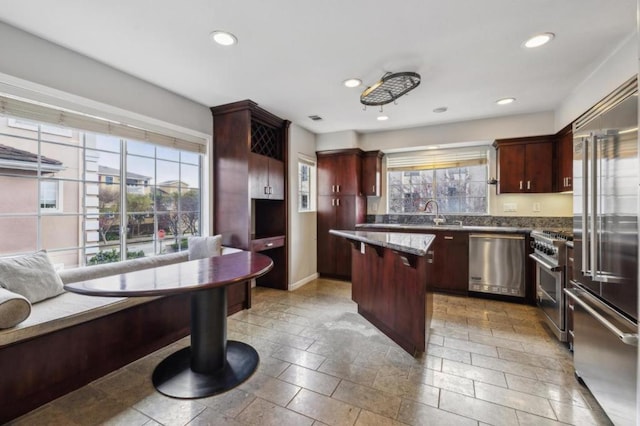 kitchen with premium appliances, a center island, dark stone counters, and sink