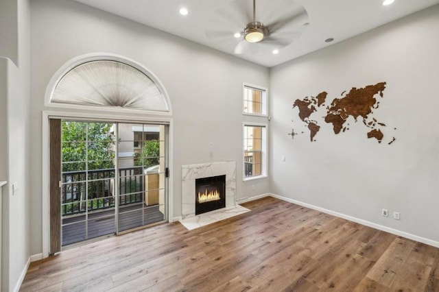 unfurnished living room with ceiling fan, a high end fireplace, wood-type flooring, and a high ceiling