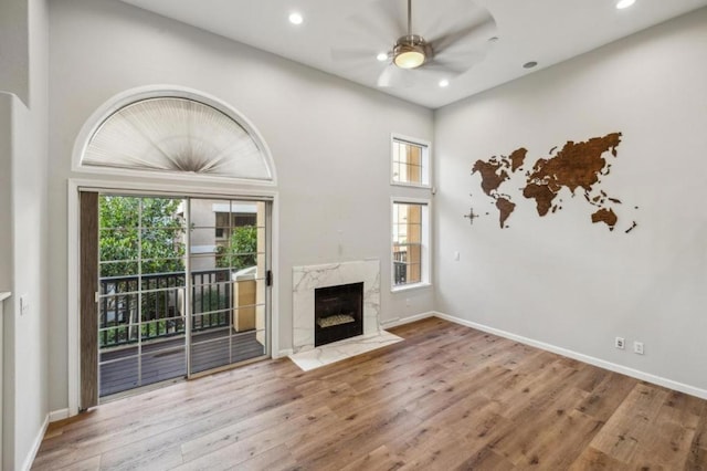 unfurnished living room with ceiling fan, wood-type flooring, a premium fireplace, and a towering ceiling