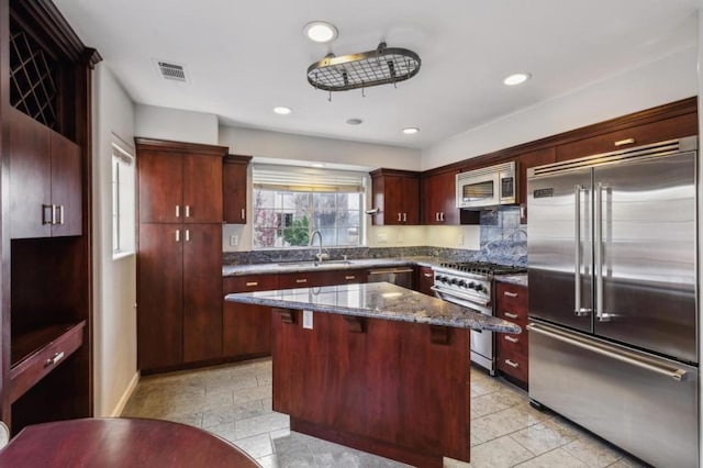 kitchen featuring a center island, dark stone counters, sink, premium appliances, and a kitchen bar