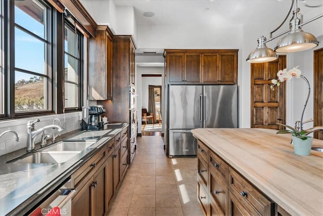 kitchen featuring pendant lighting, sink, light tile patterned floors, appliances with stainless steel finishes, and butcher block counters