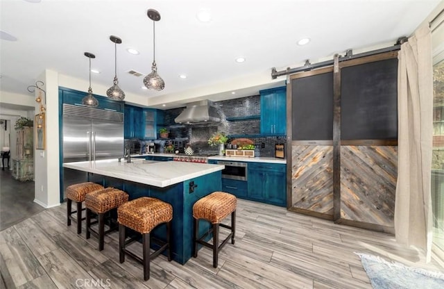 kitchen with blue cabinetry, a barn door, and wall chimney exhaust hood