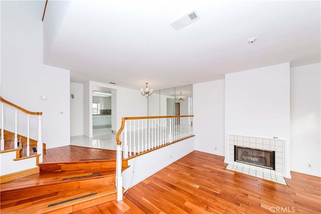 unfurnished living room featuring a tiled fireplace, light hardwood / wood-style flooring, and a chandelier