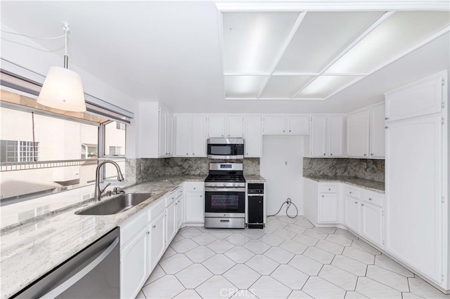 kitchen with appliances with stainless steel finishes, decorative light fixtures, white cabinetry, sink, and light stone countertops