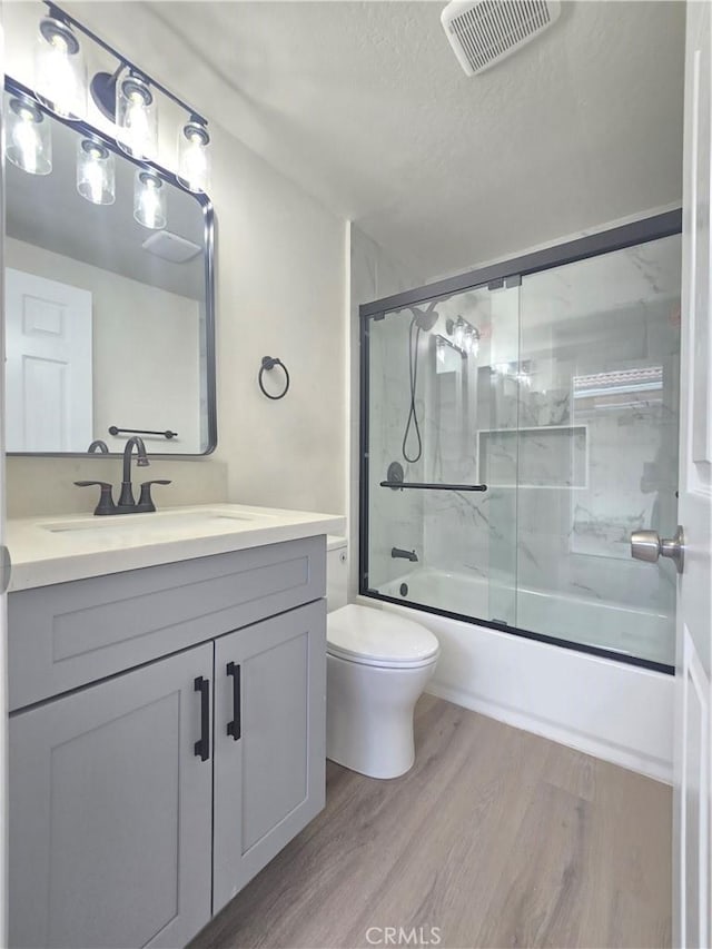 full bathroom featuring toilet, vanity, hardwood / wood-style flooring, enclosed tub / shower combo, and a textured ceiling