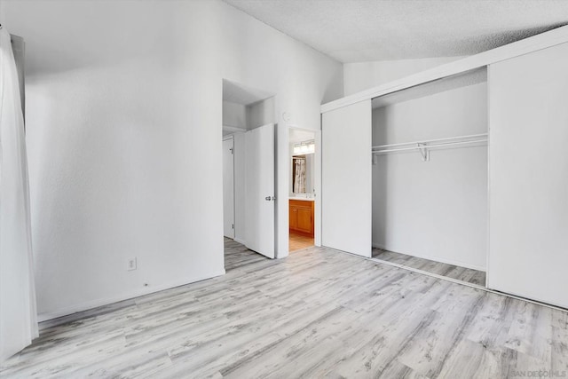 unfurnished bedroom with ensuite bath, light hardwood / wood-style flooring, a textured ceiling, vaulted ceiling, and a closet