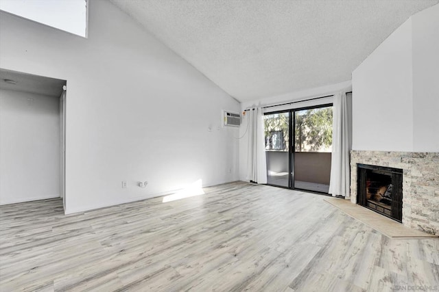 unfurnished living room featuring a stone fireplace, high vaulted ceiling, a wall unit AC, a textured ceiling, and light wood-type flooring